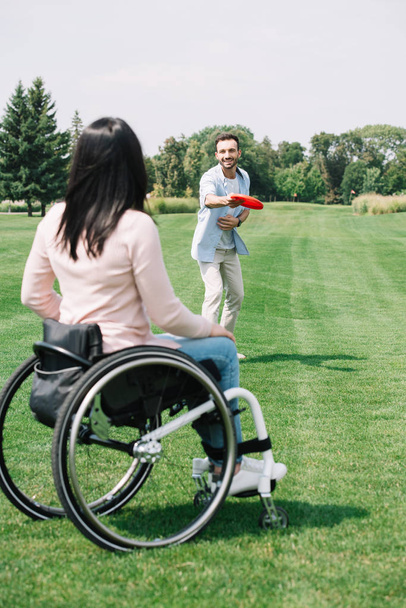 visão traseira da mulher com deficiência brincando com disco voador com namorado alegre no parque
 - Foto, Imagem