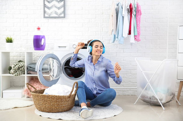 Belle jeune femme écoutant de la musique tout en faisant la lessive à la maison
 - Photo, image