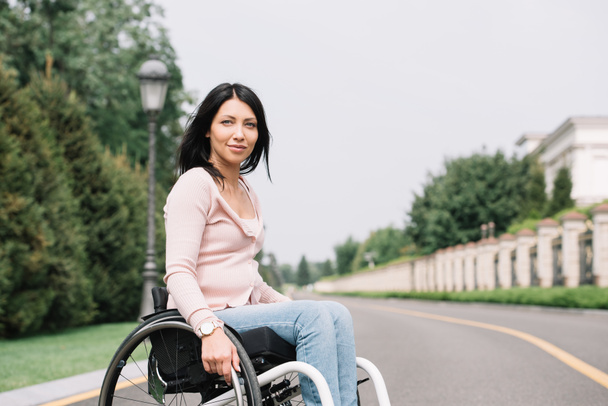 young disabled woman in wheelchair smiling and looking at camera - Fotografie, Obrázek