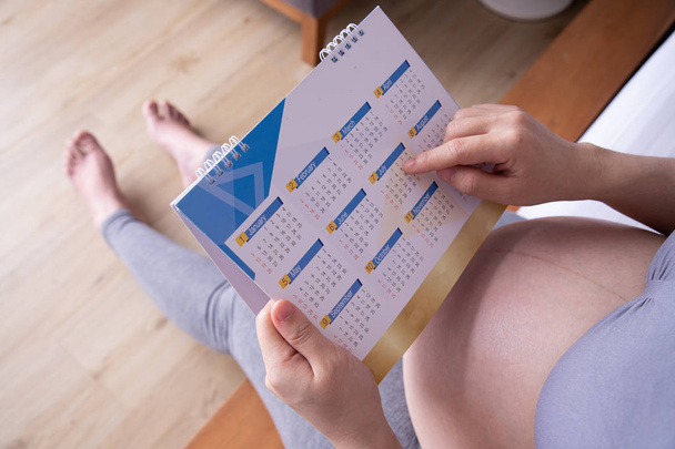 Молодая беременная женщина считает дни с календарем до рождения ребенка о
 - Фото, изображение