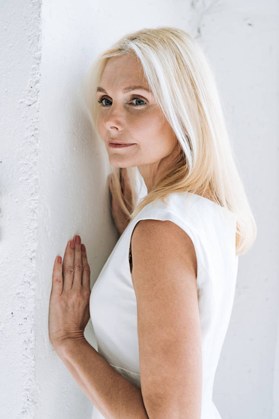 мечтательная блондинка зрелая женщина возле белой стены
 - Фото, изображение
