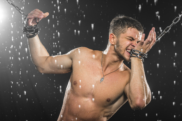 Hombre fuerte en cadenas posando bajo la lluvia, aqua studio
 - Foto, Imagen