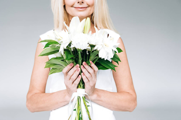 cropped view of happy blonde mature woman with white flowers isolated on grey - Φωτογραφία, εικόνα