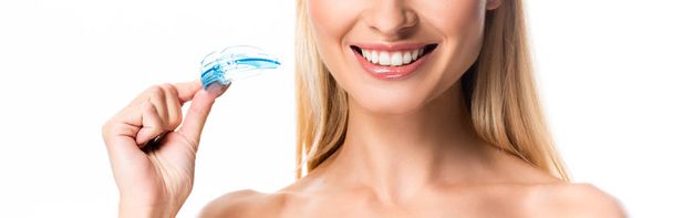 abgeschnittene Ansicht einer lächelnden blonden Frau mit weißen Zähnen, die den Mundschutz isoliert auf weiß hält - Foto, Bild