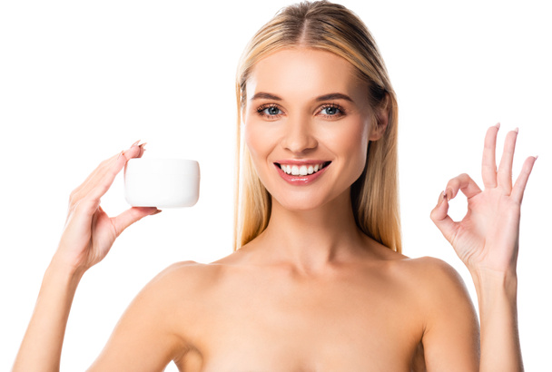 sonriente mujer desnuda sosteniendo crema cosmética y mostrando ok signo aislado en blanco
 - Foto, imagen