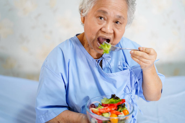 Asiatico anziano o anziano donna anziana paziente mangiare la colazione cibo sano con speranza e felice mentre seduto e affamato sul letto in ospedale
. - Foto, immagini