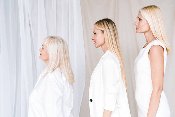vista lateral de mulheres loiras de três gerações elegantes em roupas brancas totais
 - Foto, Imagem