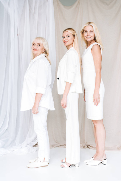 side view of elegant happy three-generation blonde women in total white outfits - Zdjęcie, obraz