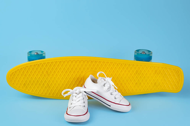 White sneakers in front of skateboard or penny board over blue background. - Foto, afbeelding