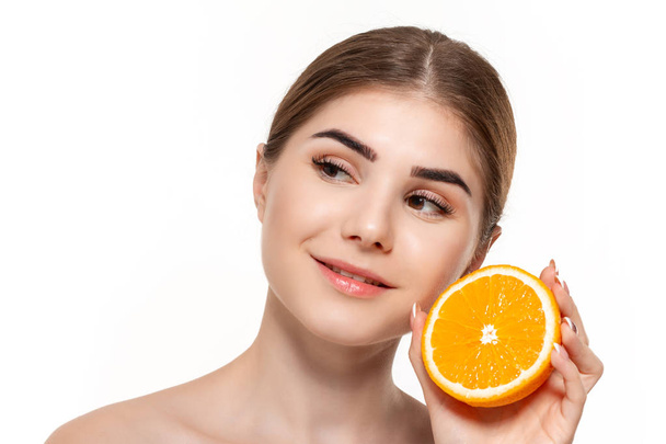 Close-up portrait of a happy beautiful young girl holding half of oranges close to face isolated over white background. Concept of beauty and health care. - Photo, Image