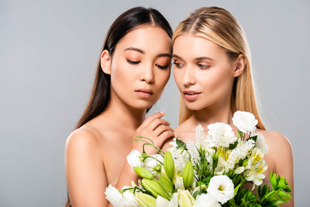tender beautiful blonde and asian brunette naked women with flowers isolated on grey - Fotó, kép