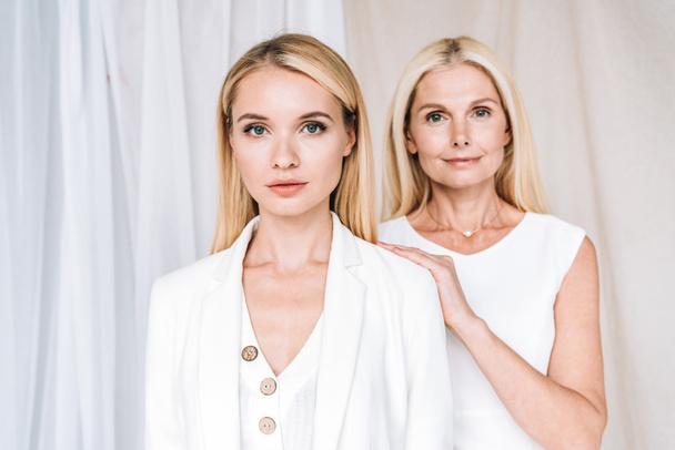elegant blonde smiling mother and serious daughter in total white outfits - Foto, Imagem
