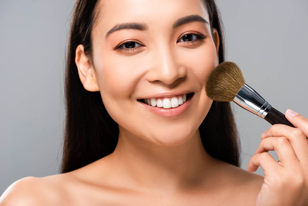 sonriendo hermosa mujer asiática desnuda con cepillo cosmético aislado en gris
 - Foto, imagen