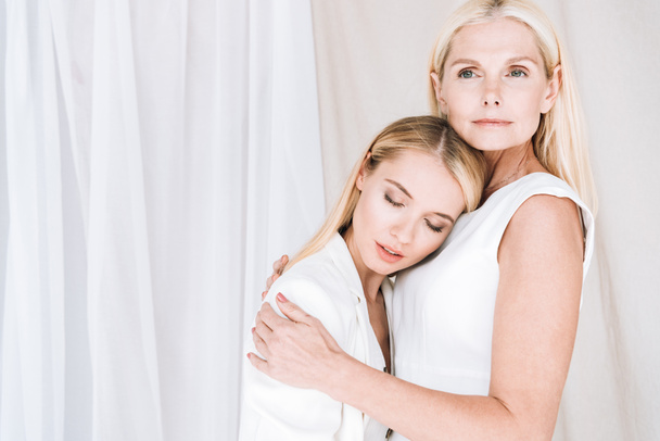 hermosa elegante rubia madre e hija abrazando sobre fondo blanco
 - Foto, imagen