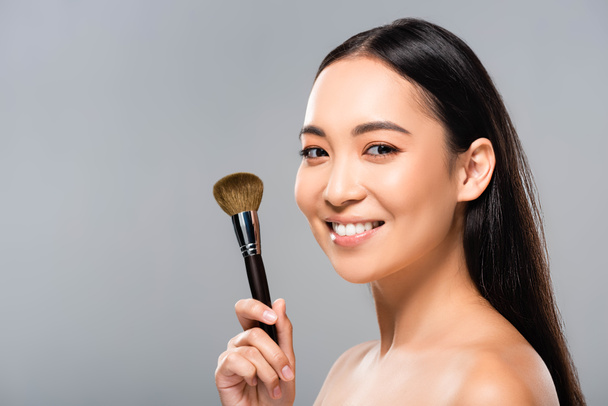 cheerful beautiful naked asian woman with cosmetic brush isolated on grey - Fotó, kép