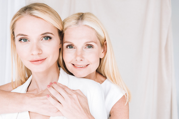 happy blonde mother and daughter in total white outfits hugging each other - Photo, Image