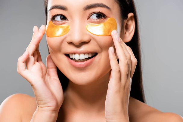 lächelnde nackte asiatische Frau mit Augenklappen im Gesicht, die isoliert von grau wegschaut - Foto, Bild