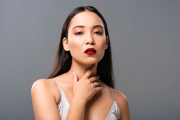 sexy asian woman in satin dress with red lips touching neck isolated on grey - Zdjęcie, obraz