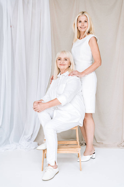 vista completa di elegante bionda figlia matura e madre anziana in abiti bianchi totali
 - Foto, immagini