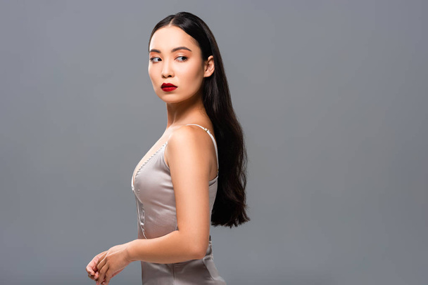 side view of beautiful smiling asian woman in satin dress with red lips isolated on grey - Fotoğraf, Görsel