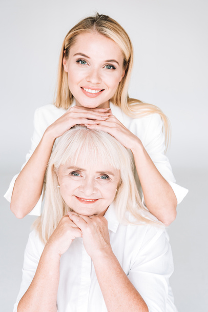 happy blonde grandmother and granddaughter in total white outfits isolated on grey - Fotoğraf, Görsel