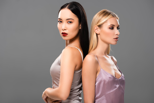 beautiful blonde and brunette women in satin dresses standing back to back isolated on grey - Photo, Image