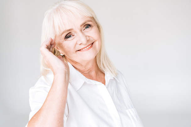 happy blonde senior woman looking at camera isolated on grey - Foto, afbeelding