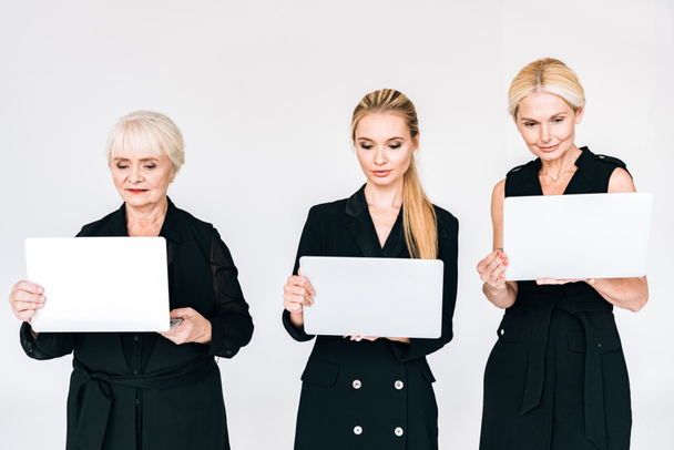 модные блондинки в трех поколениях в черных костюмах с ноутбуками, изолированными на сером
 - Фото, изображение