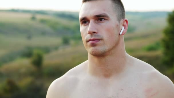 Портрет м'язистого сильного чоловіка після тренування, дивлячись на камеру, з бездротовими навушниками та голим торсом на світанку, спорт та мотивація
 - Кадри, відео