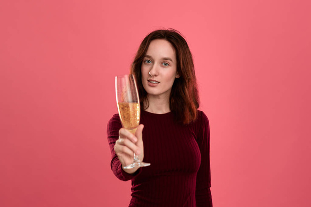 Opgewonden pretty brunette meisje Holding wijn glas mousserende Champagne staande geïsoleerd op een donkerroze achtergrond en glimlachend op de camera. - Foto, afbeelding