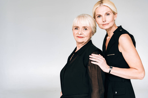 elegant blonde mature daughter and senior mother in total black outfits isolated on grey - 写真・画像
