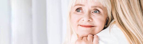 panoramatický záběr blondýny usmívající se babička jemně objímající vnučku - Fotografie, Obrázek