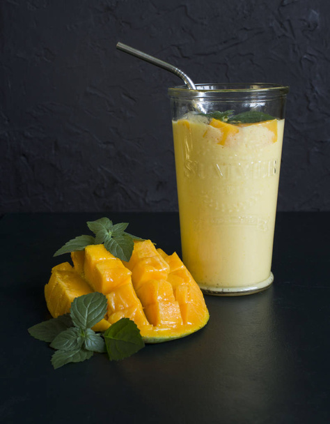 Mango Smoothie/mango Lassi w rocznika szklany kubek na ciemnej powierzchni z metalową słomką. z liści mięty i kawałek dojrzałych i soczystych mango - Zdjęcie, obraz