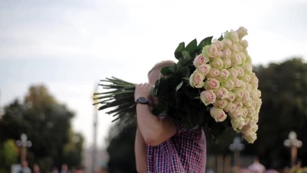 άνθρωπος με ένα μεγάλο μπουκέτο τριαντάφυλλα στον ώμο του στέκεται με την πλάτη του στην κάμερα - Πλάνα, βίντεο