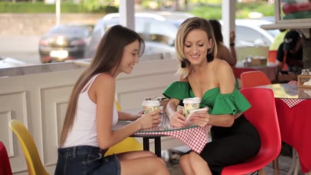 Freundinnen in einem Café sehen Fotos auf einem Smartphone und lächeln - Filmmaterial, Video