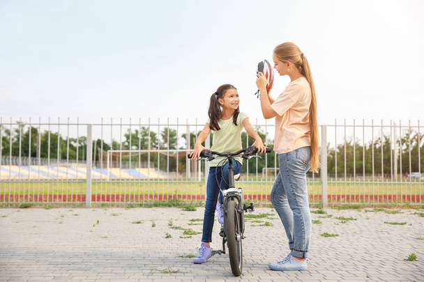 Mutter hilft ihrer Tochter, im Freien einen Fahrradhelm aufzusetzen - Foto, Bild