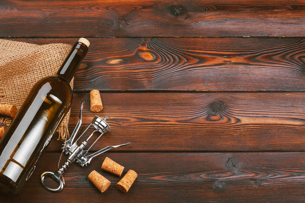 Bottle of wine and cork and corkscrew on wooden table - Foto, afbeelding