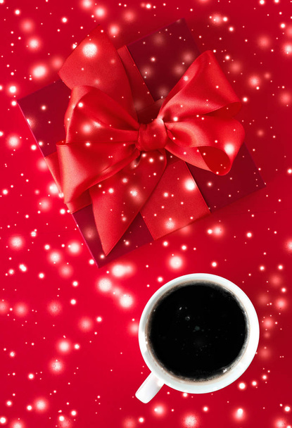 Winter holiday gift box, coffee cup and glowing snow on red flat - Photo, Image