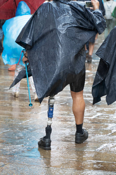 aktiver männlicher Tourist oder Pilger mit Prothese, der an einem regnerischen Tag auf einer Straße der Altstadt von Santa Cruz de Compostela spaziert - Foto, Bild