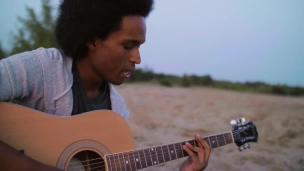 Afrikalı adam gitar çalıyor ve dışarıda şarkı söylüyor.  - Video, Çekim