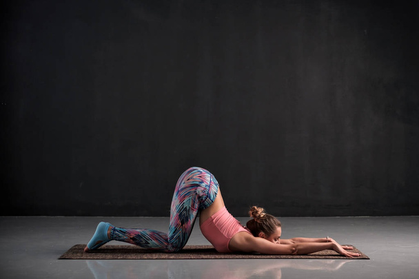 Jonge vrouw doet yoga oefening Uttana shishosana of uitgebreide puppy pose - Foto, afbeelding