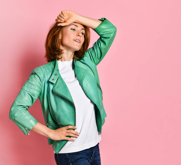 annoying and bored cute model in a green jacket leaning against a palm, standing over a pink wall with an indifferent irritated expression - Φωτογραφία, εικόνα