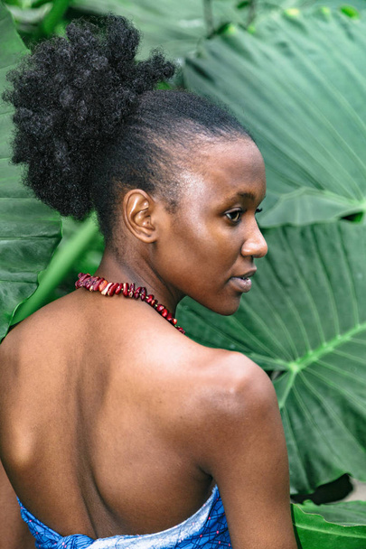 African girl half-turned against green leaves with naked back - Φωτογραφία, εικόνα