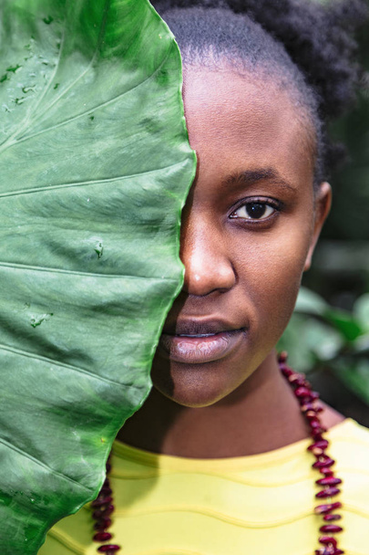 African girl with big leaf covering half of face - Foto, afbeelding