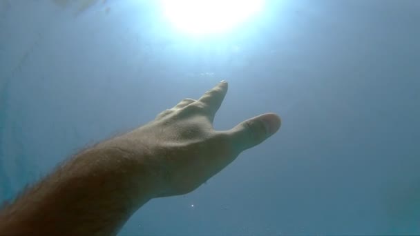De mannelijke hand strekt zich uit van onder water tot zonnestralen. Arm vraagt om hulp en probeert naar de zon te reiken. Het standpunt van de mens die verdrinkt in de zee of oceaan en naar de oppervlakte drijft. Slow motion POV - Video