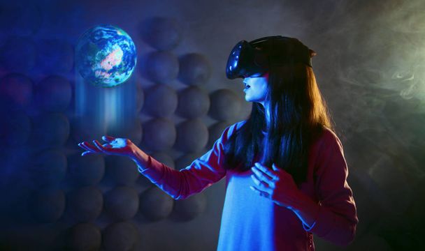 The future is in your hands. A delighted woman with virtual reality glasses holds holographic projection of the planet. - Фото, зображення