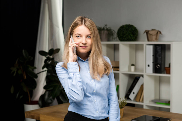 Portrait of businesswoman with mobile phone standing at office. young Caucasian businesswoman holding mobile phone in office. businesswoman using phone. Business Executive Talking On Cell Phone - Photo, Image