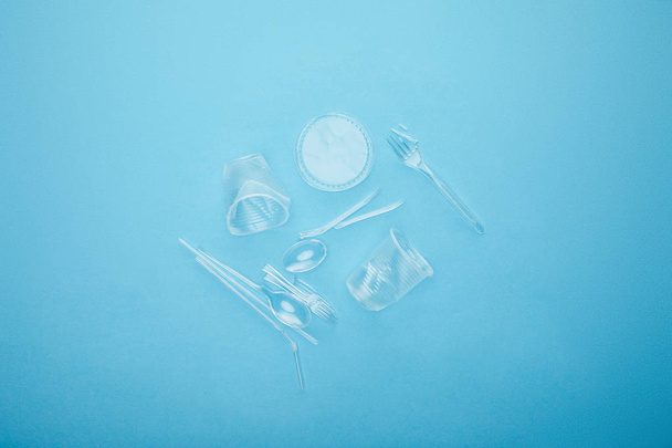 Κορυφαία όψη του σωρού από διαφανή κύπελλα μίας χρήσης, πιρούνια και κουτάλια σε μπλε φόντο - Φωτογραφία, εικόνα