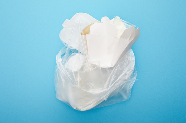 top view of plastic bag with disposable cups and containers on blue background - Фото, зображення