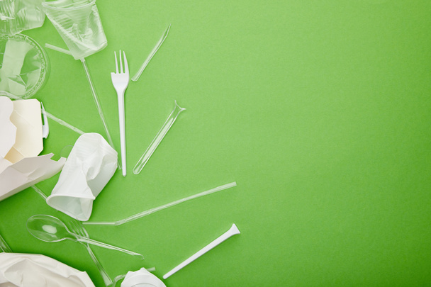 bovenaanzicht van wegwerp plastic bekers, vorken, lepels en kartonnen containers op groene achtergrond - Foto, afbeelding